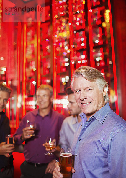 Porträt eines lächelnden reifen Mannes mit Bierglas im Nachtclub  Freunde im Hintergrund