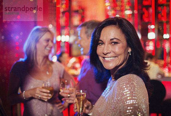 Porträt einer lächelnden Frau mit Sektflöte im Nachtclub  Menschen im Hintergrund