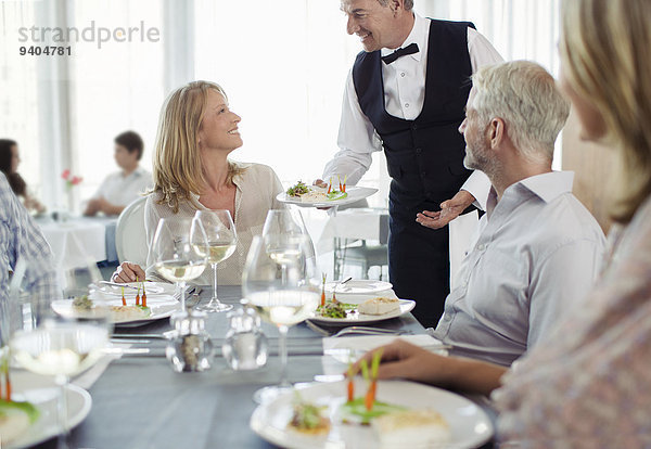 Kellner serviert der Frau  die am Restauranttisch sitzt  ein schickes Gericht.