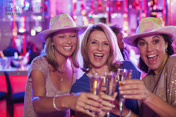 Porträt von drei fröhlichen Frauen mit Cowboyhüten und Champagnerflöte im Nachtclub