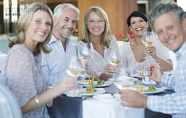 Porträt von lächelnden Menschen beim Toasten mit Weißwein im Restaurant