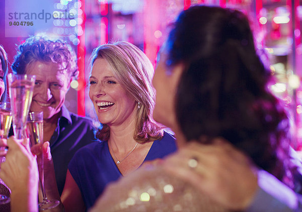 Lächelnde  reife Menschen stoßen mit Champagnerflöten im Nachtclub an.