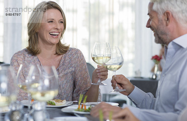 Lächelnde reife Frau und Mann beim Toasten mit Weißwein am Restauranttisch