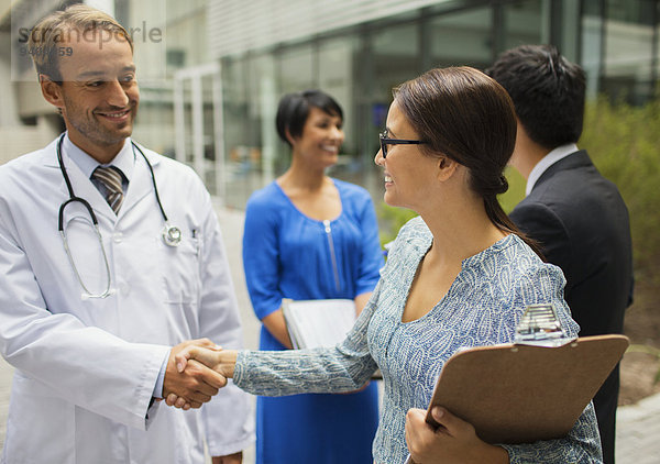 Lächelnder Arzt schüttelt Hand mit Frau vor dem Krankenhaus