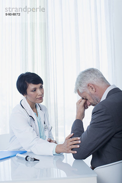 Ärztin am Schreibtisch sitzend und tröstend traurige Patientin