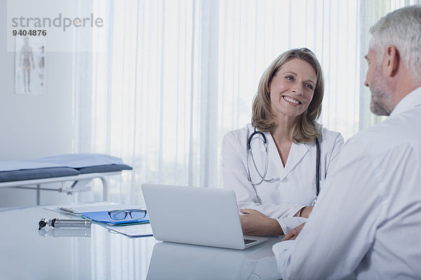 Lächelnde Ärztin im Gespräch mit Patientin am Schreibtisch im Büro