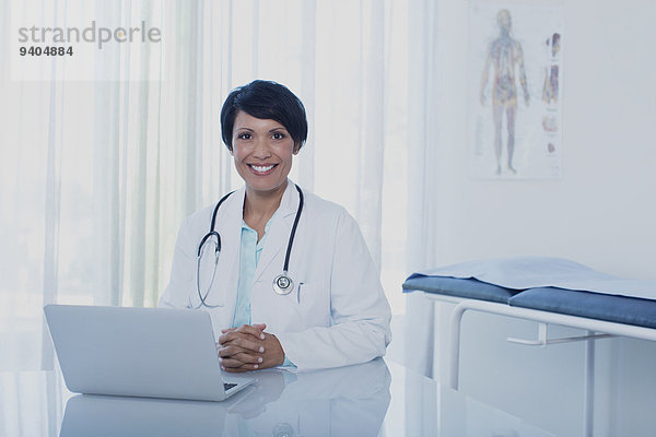 Porträt der lächelnden Ärztin am Schreibtisch mit Laptop im Büro