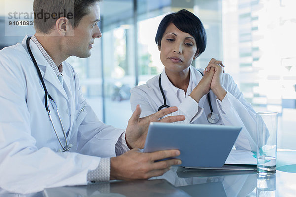 Ärzte besprechen die Behandlung des Patienten am Schreibtisch mit Hilfe eines digitalen Tabletts.