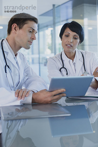 Ärzte besprechen die Behandlung des Patienten am Schreibtisch mit Hilfe eines digitalen Tabletts.