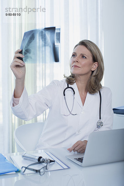Ärztin beim Röntgen am Schreibtisch mit Laptop im Büro