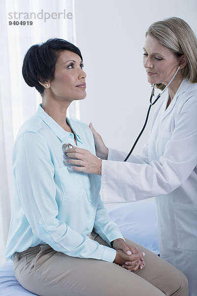 Ärztin bei der Untersuchung ihrer Patientin mit Stethoskop im Büro
