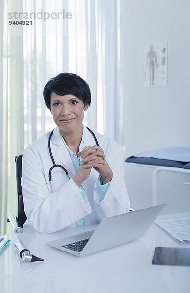 Porträt der lächelnden Ärztin am Schreibtisch mit Laptop im Büro