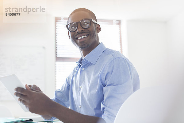 Porträt eines jungen Geschäftsmannes mit Brille und blauem Hemd mit digitalem Tablett im Büro