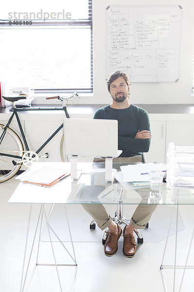 Porträt eines sitzenden Mannes mit gekreuzten Armen hinter Glas im modernen Büro  Fahrrad und Whiteboard im Hintergrund.