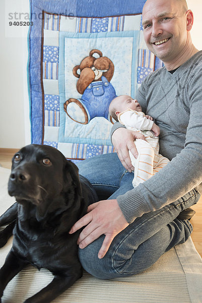 Father holding his sleeping son in his arms  dog sitting beside them