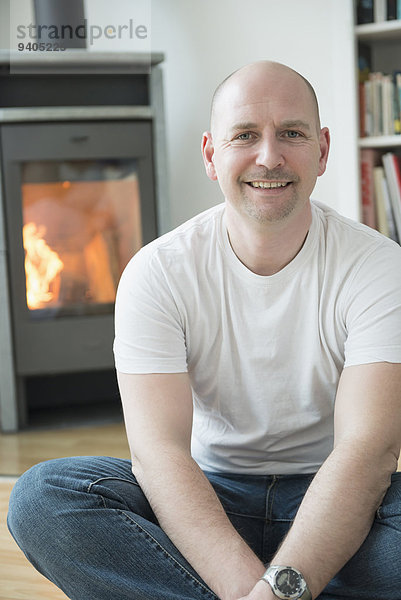 Portrait of man sitting in his living room with fireplace  smiling
