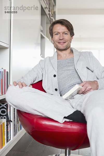 Portrait of mature man sitting on chair with book  smiling