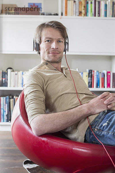 Portrait of man sitting on chair with headset and listening music  smiling