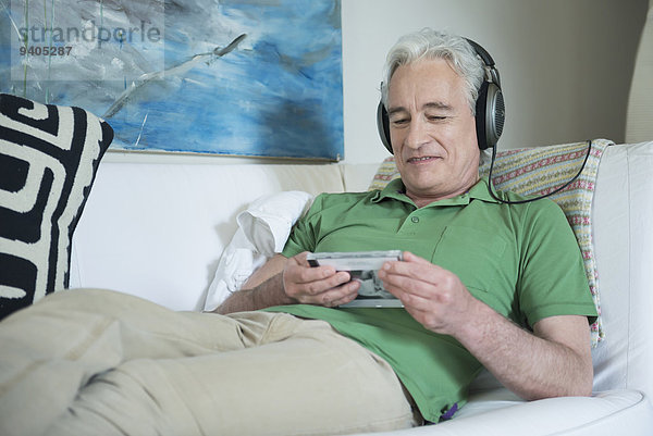 Mature man with headset sitting on couch and reading inlet of CD  smiling