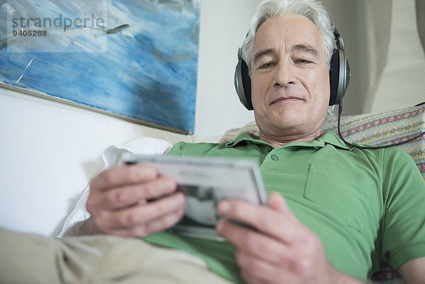 Mature man with headset sitting on couch and reading inlet of CD  smiling