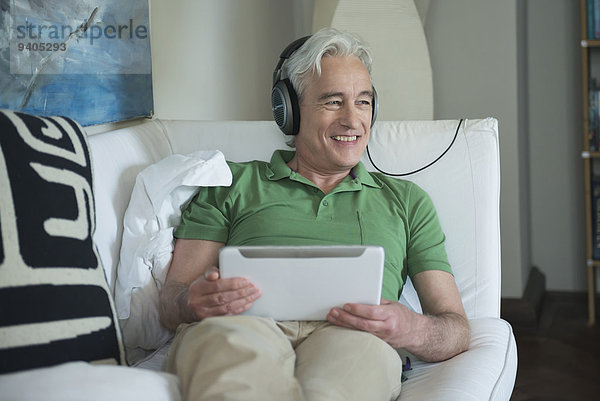 Mature man with headset and digital tablet sitting on couch  smiling