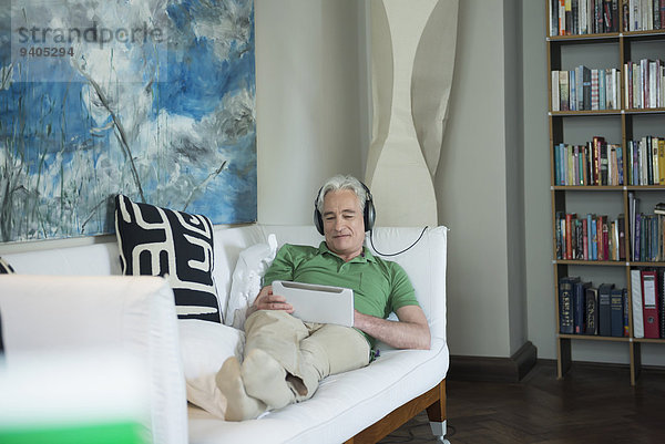 Mature man with headset and digital tablet sitting on couch  smiling