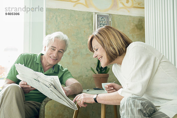 Couple reading newspaper together  smiling