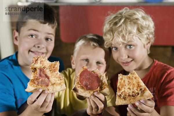 Three boys holding slices of pizza