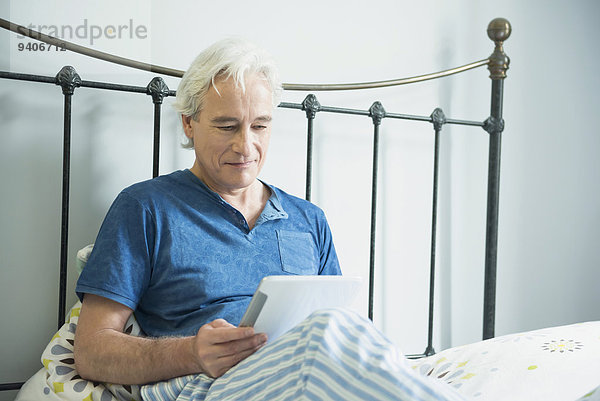 sitzend benutzen Mann lächeln Bett reifer Erwachsene reife Erwachsene Tablet PC