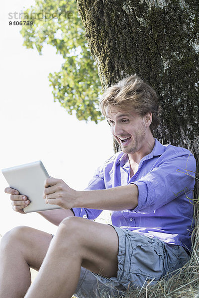 sitzend Mann lächeln Baum unterhalb Mittelpunkt Tablet PC Erwachsener