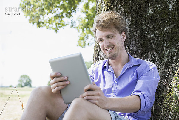 sitzend Mann lächeln Baum unterhalb Mittelpunkt Tablet PC Erwachsener