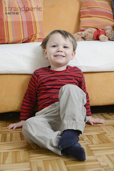 sitzend Boden Fußboden Fußböden lächeln Junge - Person frontal Couch