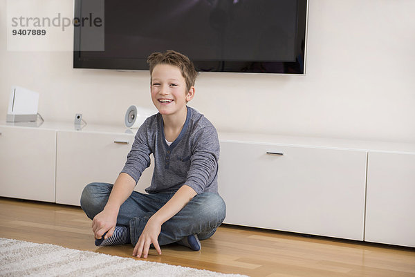 sitzend Boden Fußboden Fußböden lächeln Junge - Person Zimmer Wohnzimmer
