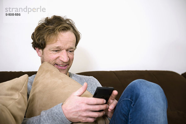 Mann lächeln reifer Erwachsene reife Erwachsene Couch Smartphone