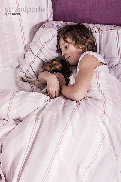 Mädchen liegt mit Dansk-Svensk Gårdshund im Bett