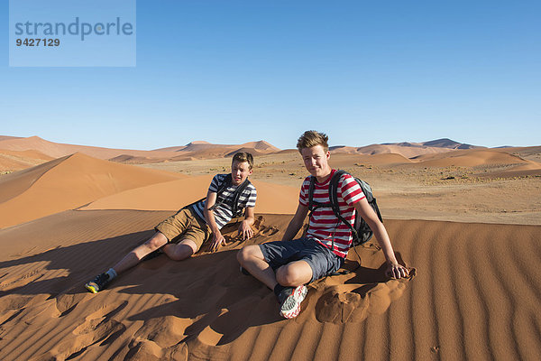 Zwei Jugendliche sitzen erschöpft auf einer Düne  Sossusvlei  Namib-Wüste  Namibia