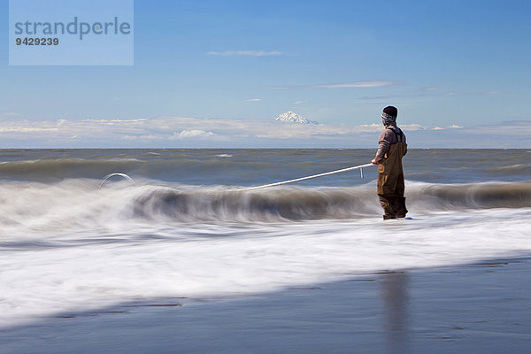 Brandungszone mit Fischer am Strand von Kenai auf der Halbinsel Kenai mit dem Vulkan Mount Redoubt am Cook Inlet in Alaska  USA.