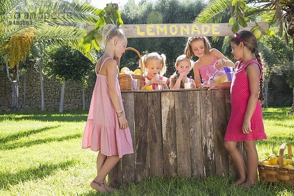 Fünf Mädchen gießen Limonade und plaudern am Limonadenstand im Park.