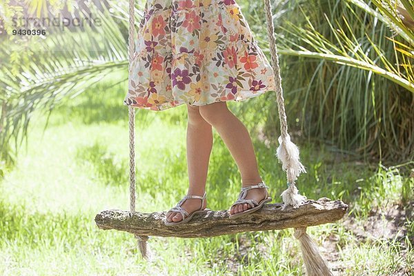 Taille unten abgeschnittene Aufnahme eines Mädchens  das auf einer Baumschaukel im Garten steht
