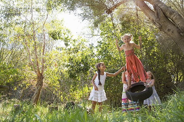 Vier Mädchen spielen auf Baumreifenschaukel im Garten