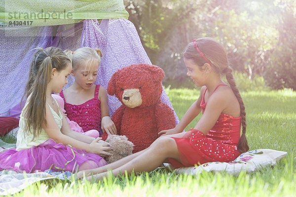 Drei Mädchen spielen mit Teddybären im Garten