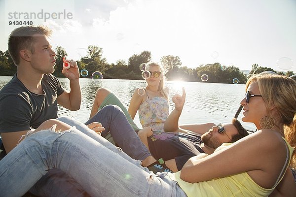 Vier junge erwachsene Freunde  die Blasen auf dem Pier am Flussufer blasen.