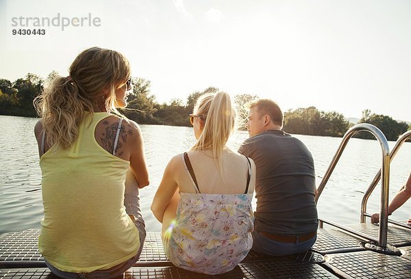 Drei junge erwachsene Freunde  die vom Pier am Flussufer blicken