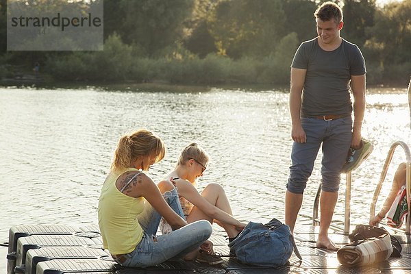 Drei junge erwachsene Freunde beim Schnürsenkelbinden am Ufer des Flusses