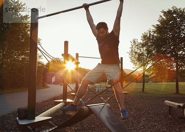 Silhouette eines jungen Mannes  der bei Sonnenuntergang auf dem Spielplatz schwingt.