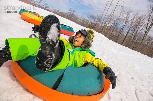 Junge lacht beim Rodeln auf schneebedecktem Hügel