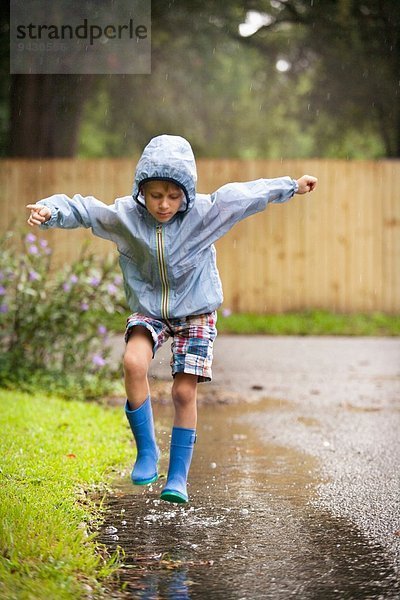 Junge in Gummistiefeln springend in der Regenpfütze