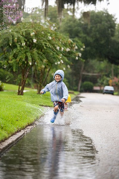 Junge in Gummistiefeln läuft und spritzt in Regenpfütze