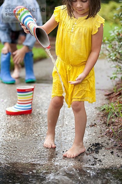 Mädchen gießt Wasser aus Gummistiefeln in die Regenpfütze