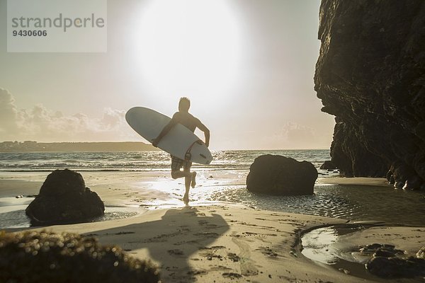 Erwachsener Mann  der zum Meer rennt und Surfbrett hält